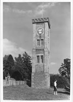 A clock tower with a person standing on a hill

Description automatically generated